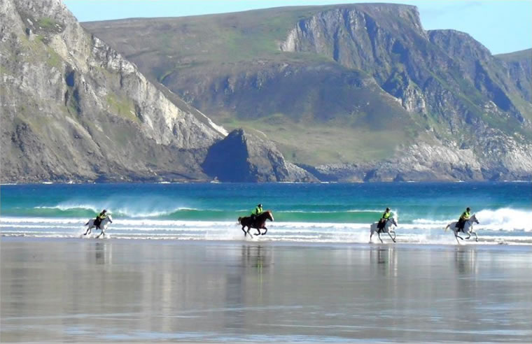 Horses gallop on Keel beach with Minaun in background