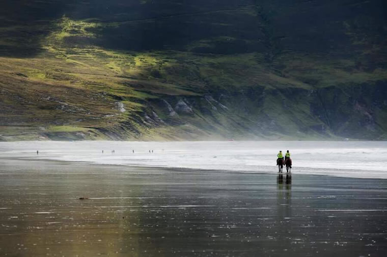 Two horses trotting in Keel beach with Dookinella cliffs in background